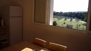 Une pièce comprenant une table à manger et des chaises, une fenêtre donnant sur un paysage verdoyant et un réfrigérateur blanc.