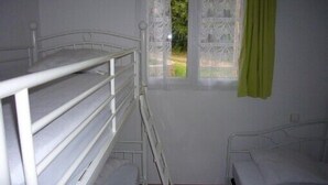 Une chambre avec un lit superposé et un lit simple, une fenêtre ornée de rideaux en dentelle et une vue sur la verdure environnante.