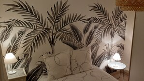 A bedroom with a bed, a nightstand, a bedside table, and a wall with a tropical leaf pattern. - The closeau du cèdre in Normandy between Paris and Rouen, near Giverny (Ménilles)