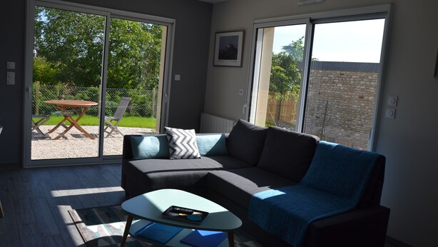 A modern living room with a sectional sofa, a glass coffee table, and a sliding glass door leading to a patio area. - The closeau du cèdre in Normandy between Paris and Rouen, near Giverny (Ménilles)
