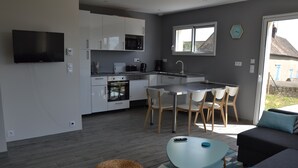 A modern kitchen with white cabinets, a microwave, and a dishwasher. There is a dining area with a table and chairs. A TV is mounted on the wall. - The closeau du cèdre in Normandy between Paris and Rouen, near Giverny (Ménilles)