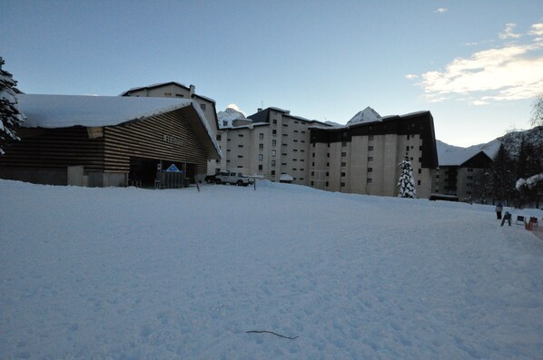 A snow-covered landscape with a large building featuring multiple windows and a sloped roof.