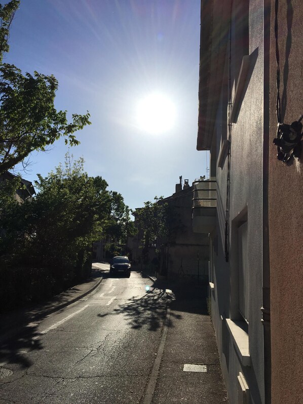 Una estrecha calle urbana con un coche aparcado, árboles y edificios.