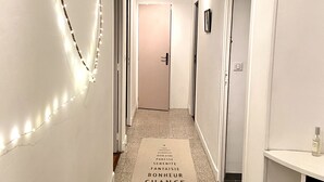 Un pasillo con una decoración luminosa en forma de corazón en la pared, una tira de luces y un felpudo con palabras en francés.