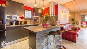 A modern kitchen with a central island, bar stools, a red sofa, and a large window. - Chalet Haute Savoie quiet jacuzzi wifi near Lake Annecy (Thônes)