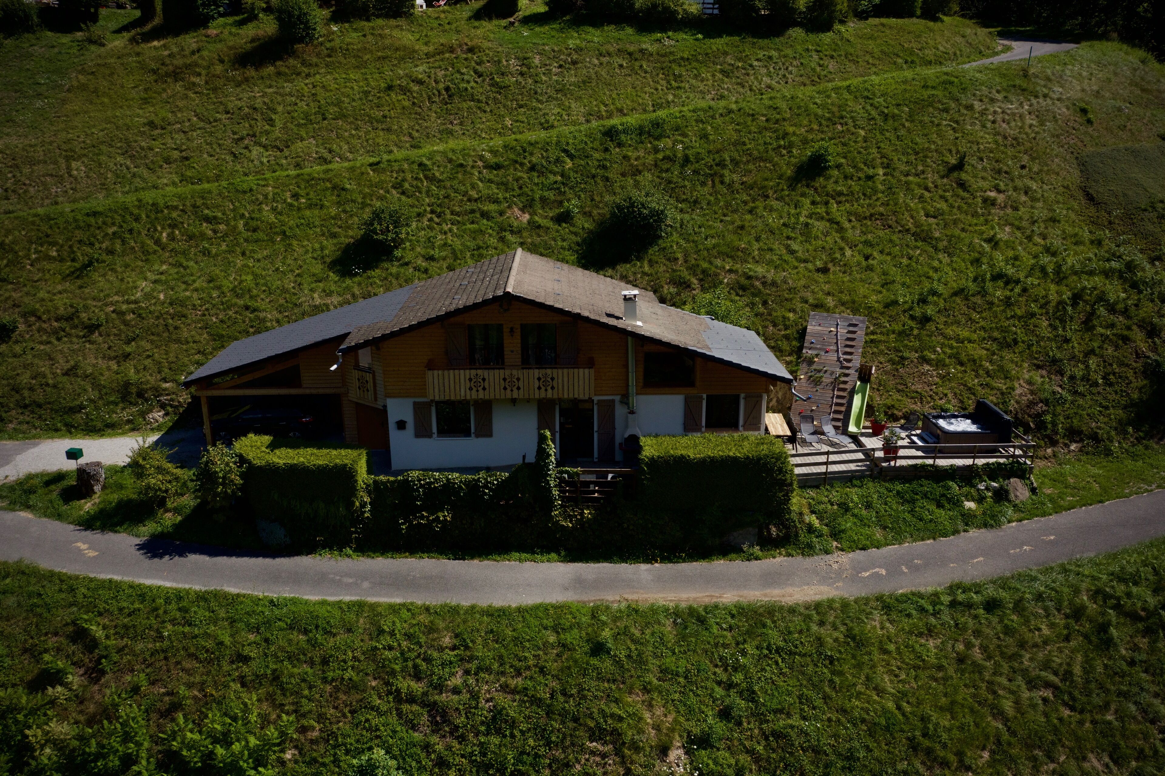 A two-story house with a sloped roof, surrounded by lush green hills.