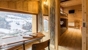 A wooden interior with a table and chairs, a bunk bed, and a window with a snowy landscape view. - Chalet Haute Savoie quiet jacuzzi wifi near Lake Annecy (Thônes)