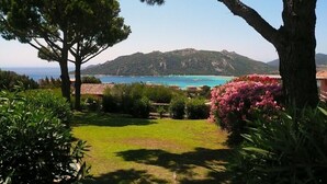Un paisaje costero con una zona verde, árboles y vistas al mar y a las montañas.