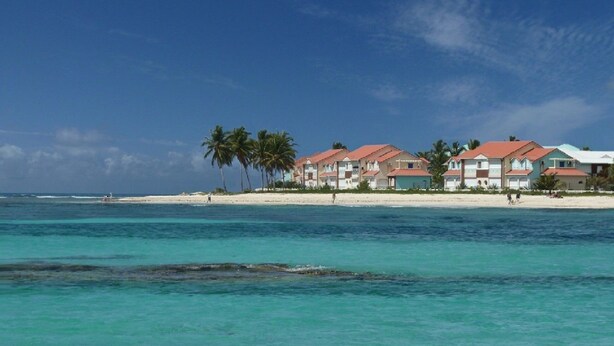 Ett hotell vid stranden med flera byggnader, palmer och kristallklart turkosfärgat vatten.