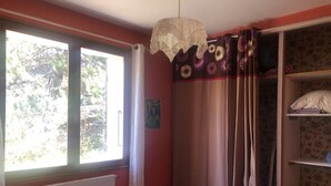 Un dormitorio con una ventana grande, un radiador, una cama y un armario con estantes.