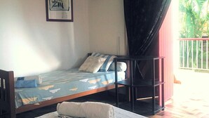 Una cama individual con una colcha azul y blanca estampada, una almohada y una toalla enrollada sobre un cabecero de madera. Un cuadro enmarcado cuelga en la pared sobre la cama.