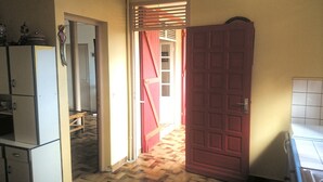 Un pasillo con suelo de madera, una puerta roja y una zona de cocina con armarios y un refrigerador.