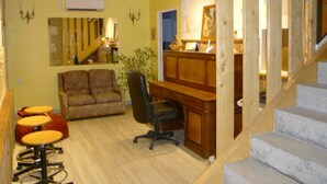 Quarto com escrivaninha de madeira, sofá marrom, cadeira de escritório preta e pequena mesa de jantar com banquetas.
