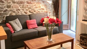 Ein Wohnzimmer mit Steinwand, einem grauen Sofa mit roten und grauen Kissen, einem Holztisch und einer Vase mit Blumen.