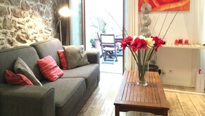 Ein Wohnzimmer mit einer Steinwand, einem grauen Sofa mit roten und beigen Kissen, einem Holztisch mit einer Vase voller roter und weißer Blumen und einem großen Gemälde einer Rose an der Wand.