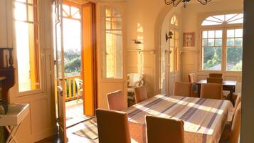 Een eetkamer met een tafel voor vier personen, een kroonluchter en uitzicht door de geopende deur.