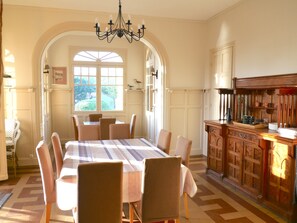 A dining area with a table set for six, surrounded by chairs, a chandelier, and a view through an arched window.