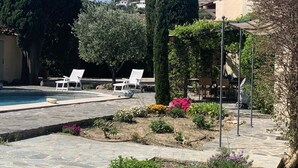 A pool area with stone flooring, white lounge chairs, and a variety of plants and flowers. - Charming farmhouse in a 5000m2 field, private swimming pool, beach 200m away (Sainte-Maxime)