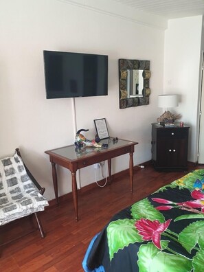 Una habitación con cama, televisor, escritorio con silla, cómoda y espejo.
