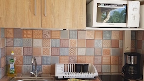 Een keuken met houten kastjes, een magnetron, een koffiezetapparaat, een spoelbak en een betegelde achterwand.