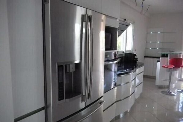 A modern kitchen with stainless steel appliances, a glass countertop, and a bar area with red stools.