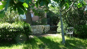 A garden with a stone wall, a metal chair, and a tree.