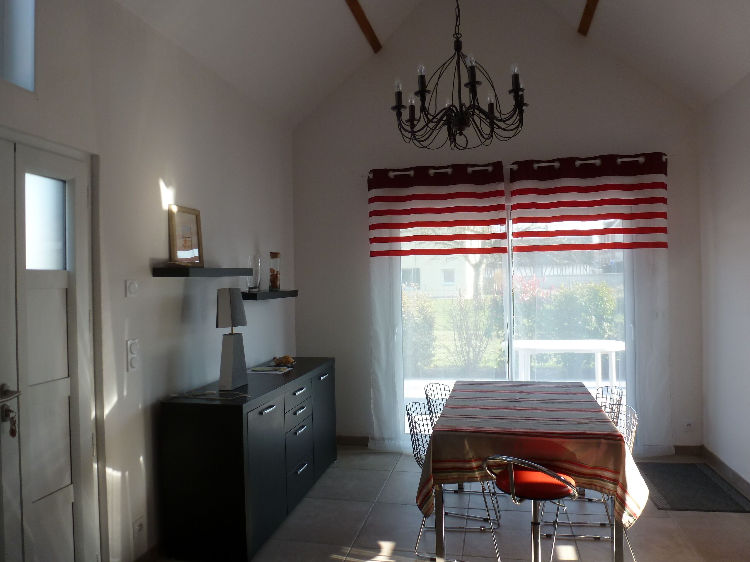 Un coin repas comprenant une table, des chaises, un lustre et une fenêtre ornée de rideaux à rayures.