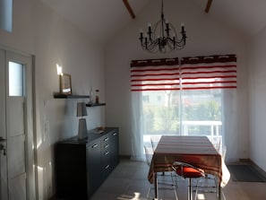Uma sala de jantar com mesa, cadeiras, um candelabro e uma janela com cortinas listradas.
