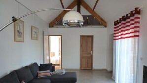 A living room with a dark-colored sofa, a glass coffee table, a ceiling fan, and a wooden door.