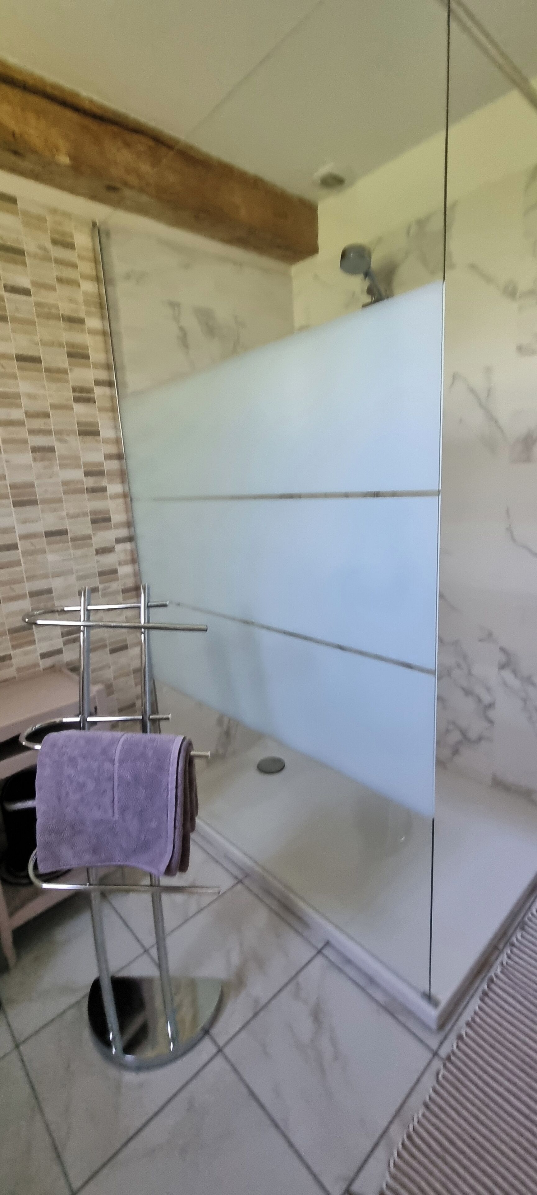 Un baño con cabina de ducha de vidrio, un perchero con una toalla morada y piso de baldosas de mármol.