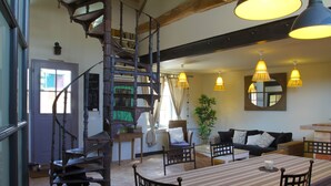 Un vaste espace de vie agrémenté d’un grand escalier en bois, d’une table à manger avec des chaises, d’un canapé et de luminaires suspendus.