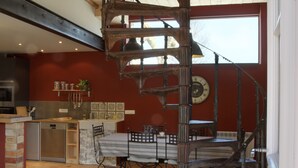 Une cuisine avec un escalier en colimaçon, une table à manger et une horloge au mur.
