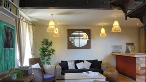 Un salon chaleureux avec un canapé noir, des fauteuils en osier, une table basse et des lampes suspendues.