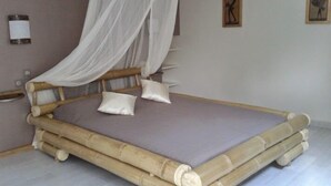 Een kamer met een bed met een bamboeframe en een hemelbed.