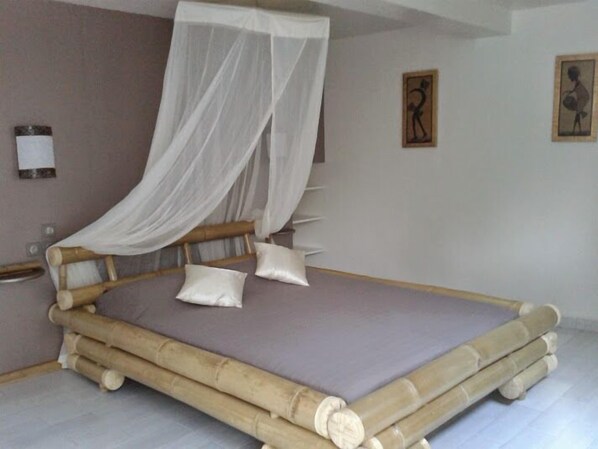 A room with a bed featuring a bamboo frame and a canopy. - Apartment "ARBRE VOYAGEUR", swimming pool, mountain view (PETIT-BOURG)