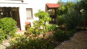 A garden with various plants and a building with a red roof and barred windows.