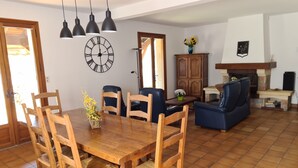 A dining area with a wooden table and chairs, a clock on the wall, and a fireplace in the background. - Charming holiday home with private heated pool (Prayssac)