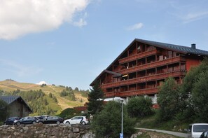A multi-story wooden building with balconies, surrounded by trees and parked cars. - APARTMENT CRYSTAL SNOW (Hauteluce)
