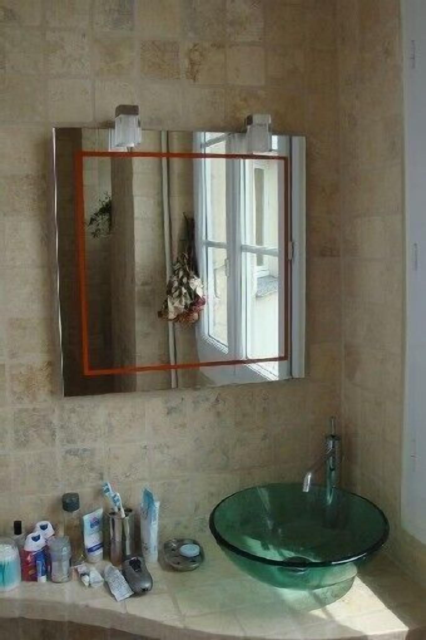Ein Badezimmer mit einem Glaswaschbecken, einem Spiegel und Pflegeprodukten auf der Ablagefläche.