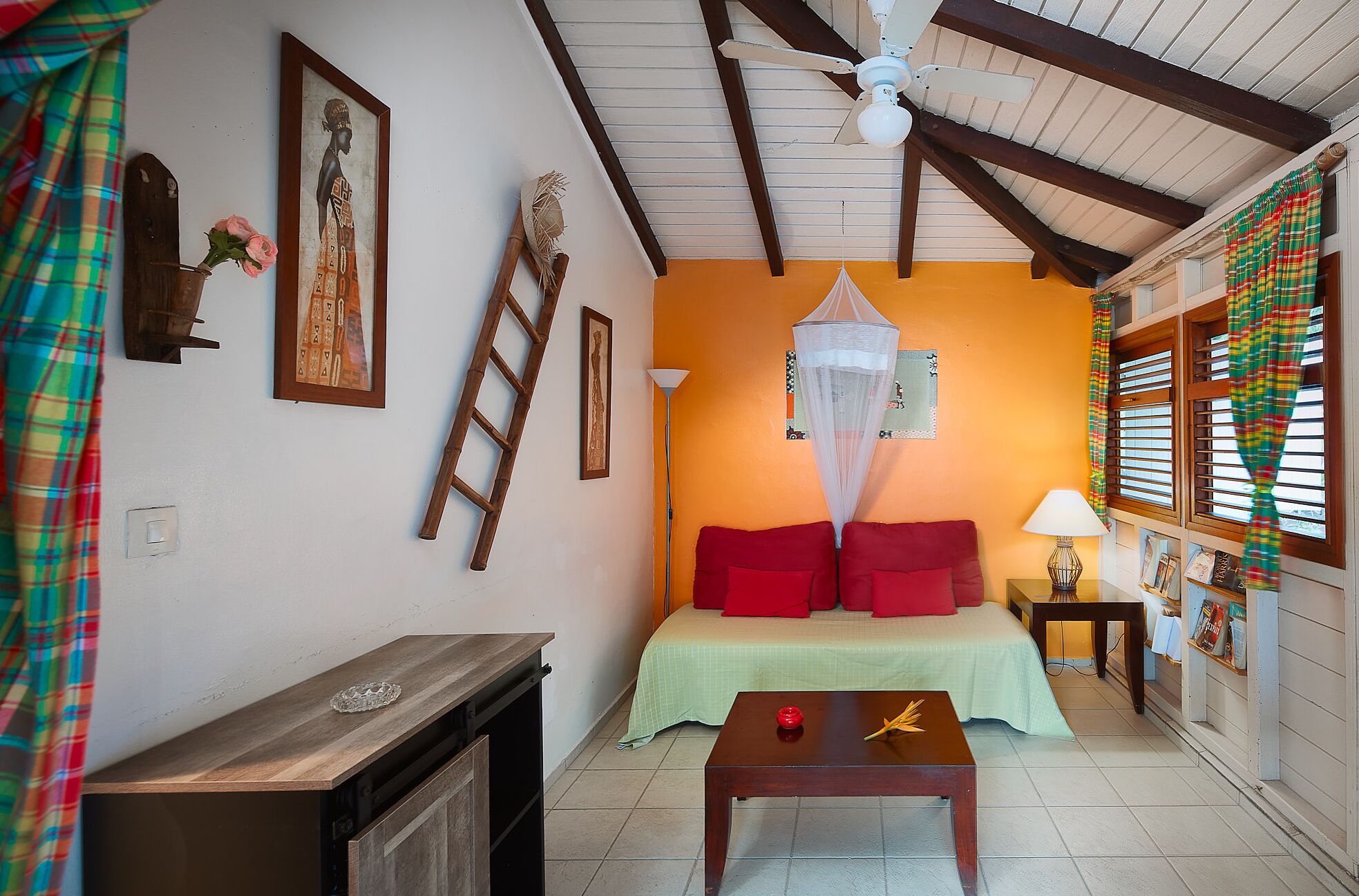A room with a bed, a nightstand, a table, a ladder, and a window with curtains.