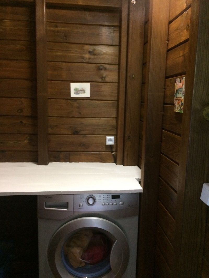 A compact laundry area with a front-loading washing machine and a wooden wall with a small electrical outlet.