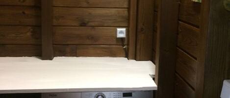 A compact laundry area with a front-loading washing machine and a wooden wall with a small electrical outlet.