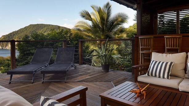 A wooden deck with lounge chairs and a sofa, surrounded by lush greenery and a view of a mountain. - Villa Kaz Coco, sea views (Deshaies)