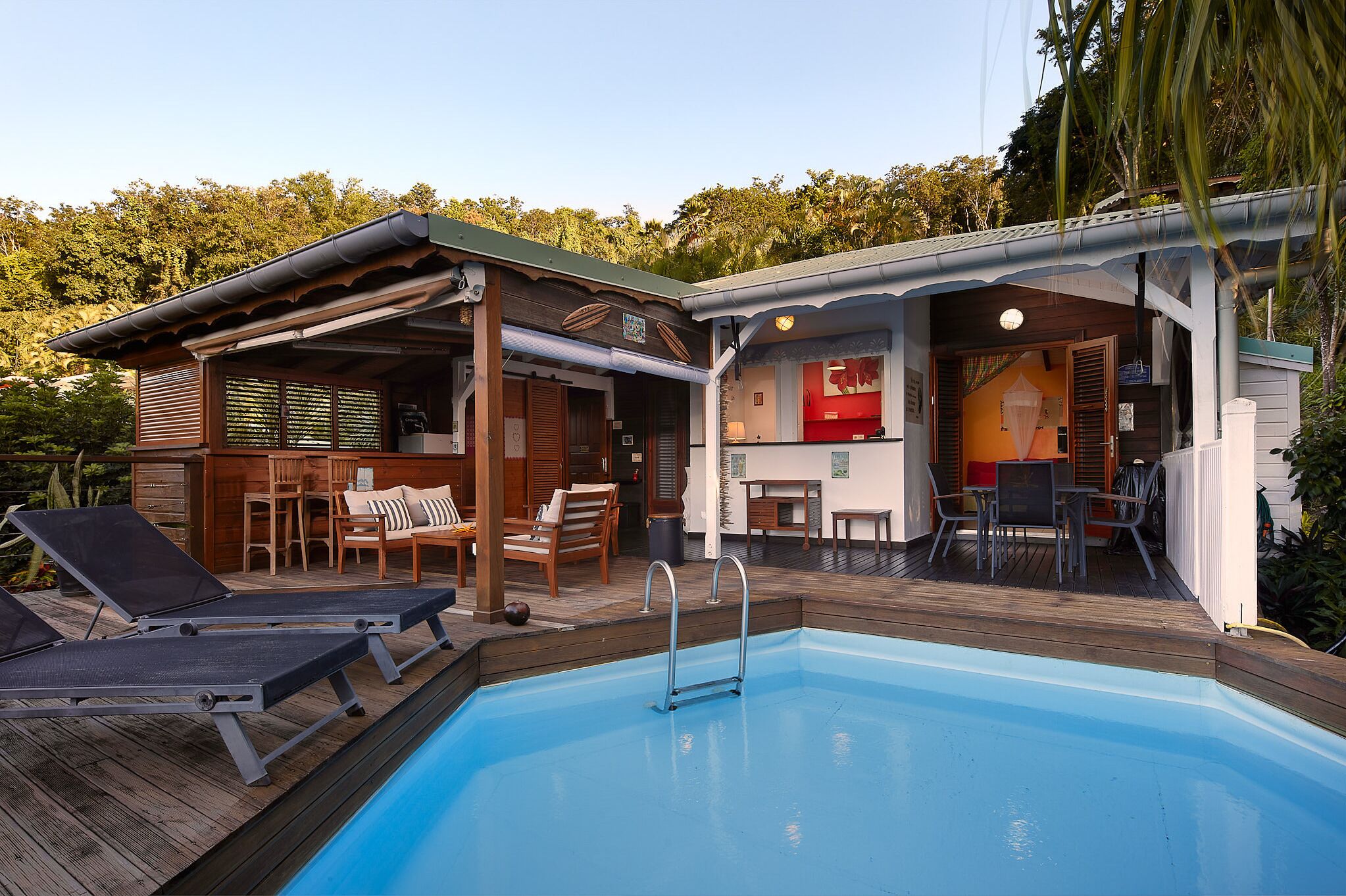 Un espace aménagé au bord de la piscine, avec des chaises longues, un barbecue et un petit bâtiment sur lequel on peut voir une enseigne rouge.