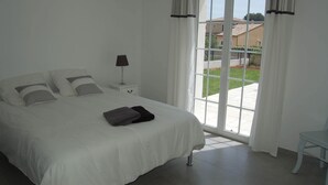 A bedroom with a large bed, a nightstand, a lamp, and a view of the outside through a sliding glass door. - Air-conditioned villa with heated pool for 9 people (La Motte)