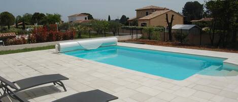 A swimming pool with lounge chairs and a tiled deck.