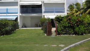 A two-story building with a white facade and blue railings, surrounded by well-maintained greenery and a clear sky. - Very nice F2 facing the sea, direct access to Sainte-Anne beach, swimming pool, tennis (SAINTE ANNE)