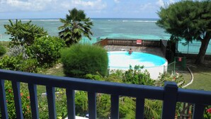 A swimming pool with a view of the ocean, surrounded by greenery and a wooden deck. - Very nice F2 facing the sea, direct access to Sainte-Anne beach, swimming pool, tennis (SAINTE ANNE)