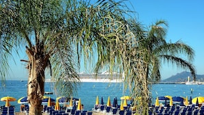 A beach with rows of blue chairs and yellow umbrellas, palm trees, and a cruise ship in the background. - NEW !! ''CANNES-CENTER'' Cosy  high standing apartment in the heart of Cannes (Cannes)