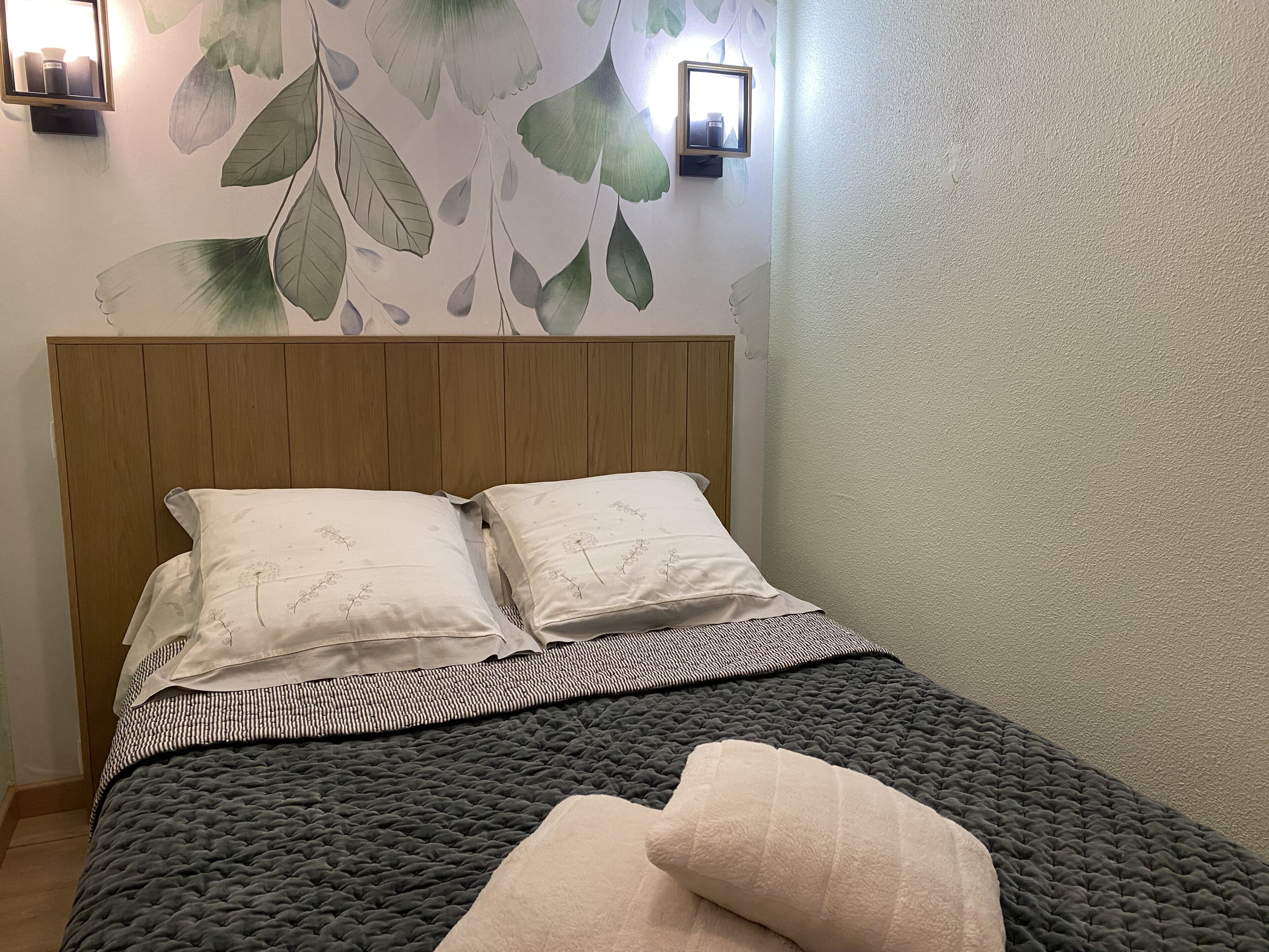 Een net opgemaakt bed met een donkere quilt, twee kussens en een gebatoofd dekbed.